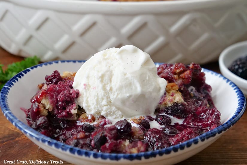 A horizontal photo of a serving of berry cobbler with a scoop of vanilla ice cream on top.