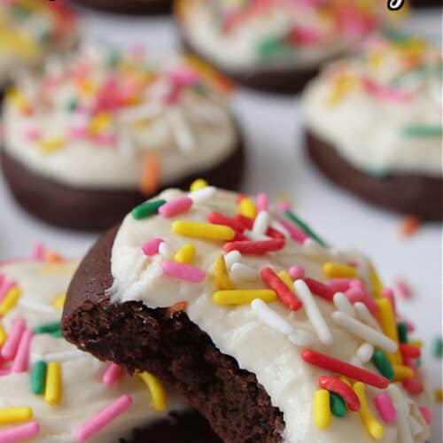 A few brownie cookies with white frosting and jimmie candy sprinkles on top with a bite out of one of the cookies.