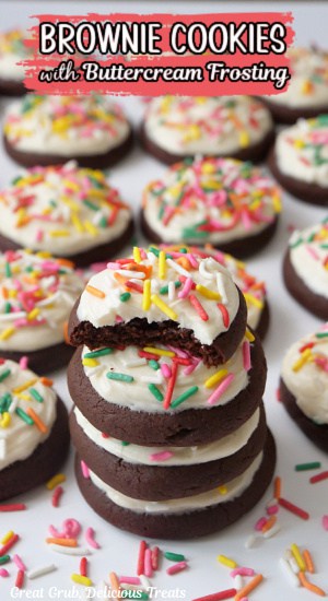 A white surface with a couple dozen cookies on it that have white frosting and jimmie sprinkles on top.