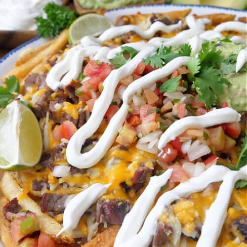 A close up of a plate full of carne asada fries topped with sour cream.