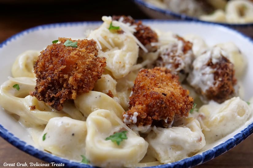 A horizontal photo of a white bowl with blue trim filled with a serving of fried chicken tortellini alfredo.