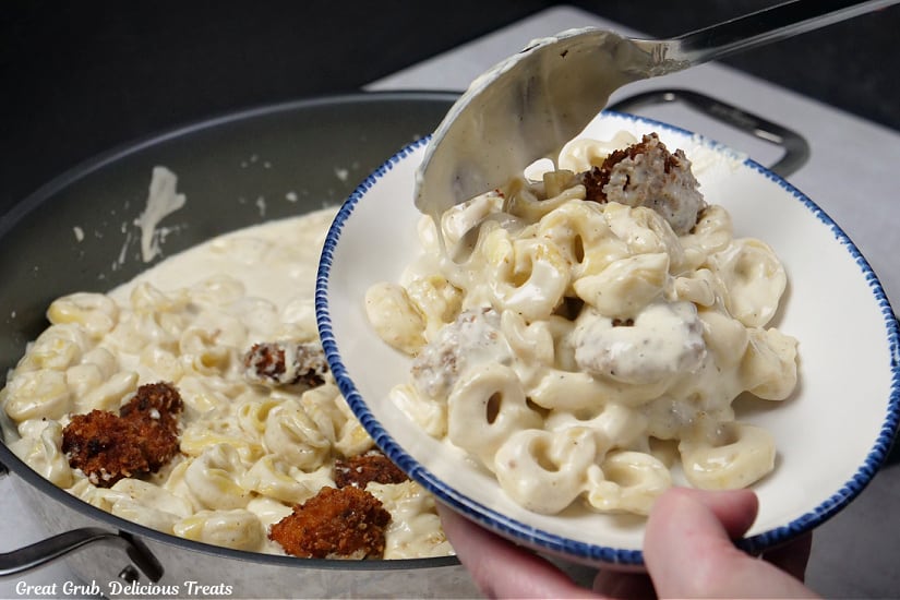 A horizontal photo of a white bowl with blue trim and the electric skillet underneath and a serving of chicken tortellini alfredo being spooned into the bowl.