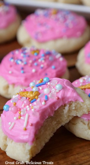 A few soft sugar cookies with pink frosting and candy sprinkles with a bite taken out of one of them.