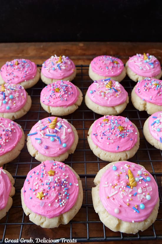 A wire rack with pink frosted sugar cookies with candy sprinkles on top.
