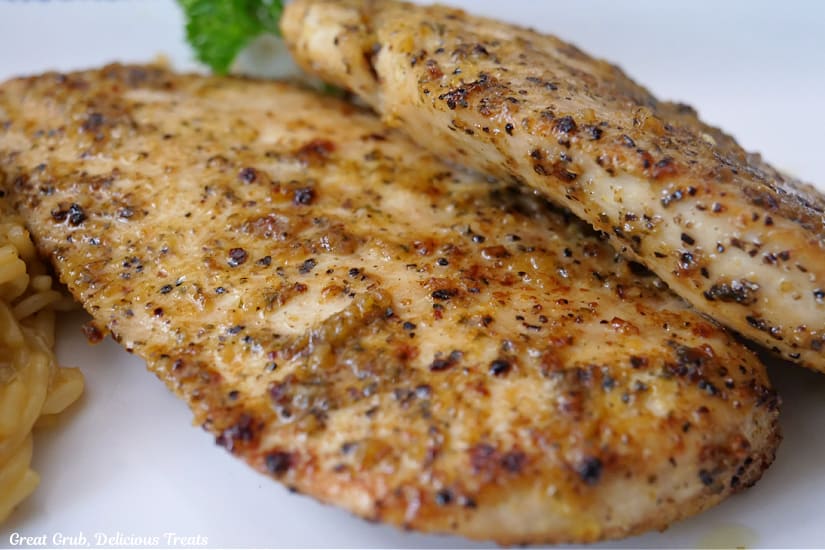 Two pieces of lemon pepper chicken breasts on a white plate.