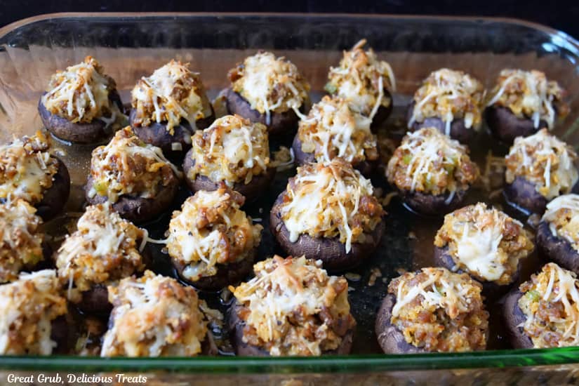 A glass baking dish with 24 stuffed mushrooms in it after being pulled out of the oven.