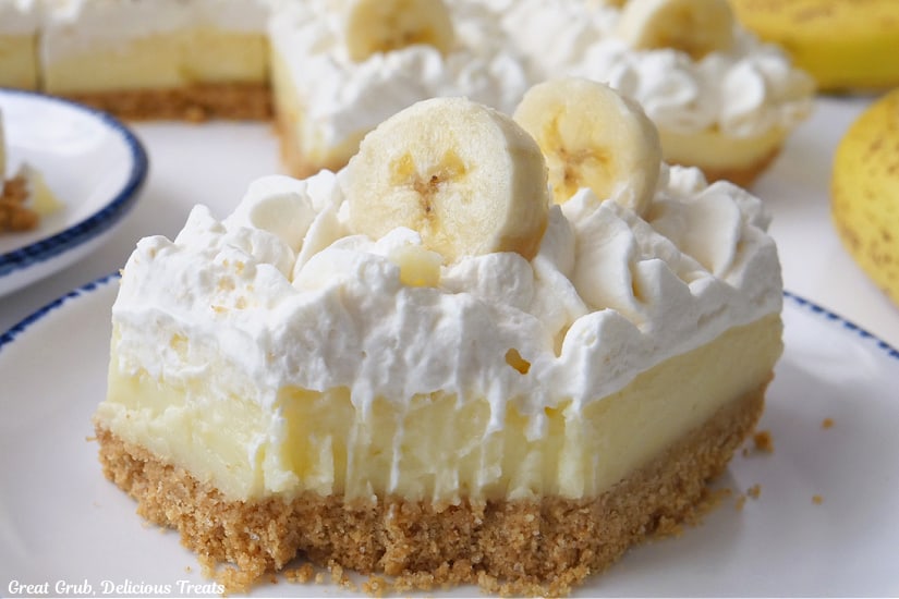 A horizontal photo of a white plate with blue trim with a serving of banana bar on it and a bite has been taken out.