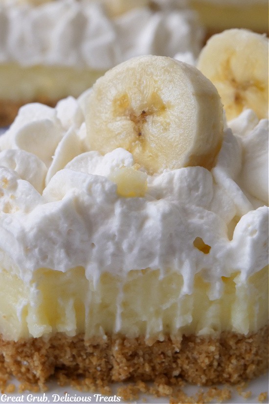 A super close up of a banana bar showing the graham cracker crust, the banana filling and the whipped cream topping.