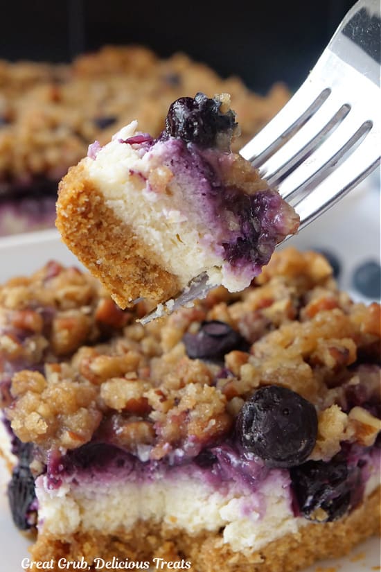 A close up of a bite of blueberry cheesecake bar on a fork.
