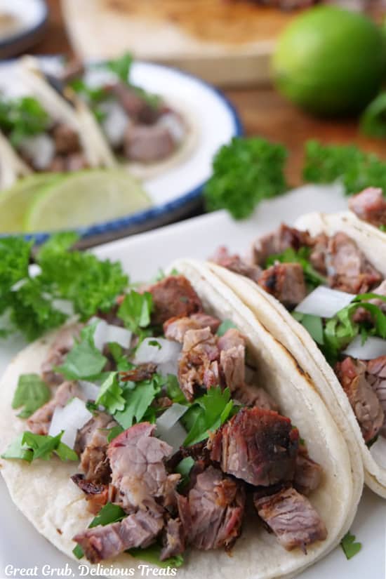 A close up of two carne asada street tacos on a white plate.