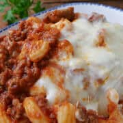 A white bowl with blue trim filled with a serving cheesy pasta with ground beef and Italian sausage.
