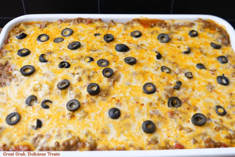 A horizontal photo of a white deep dish baking dish filled with Mexican Lasagna after being pulled out of the oven.