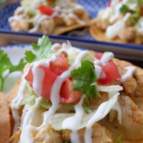 A close up of a mini chicken tostada with lettuce, diced tomatoes, sour cream and cilantro.