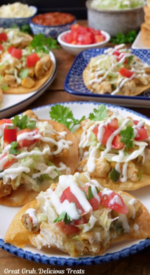 A white plate with blue trim with three mini tostadas on it with more in the background.