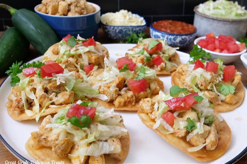A large white plate with seven mini chicken tostadas on it.