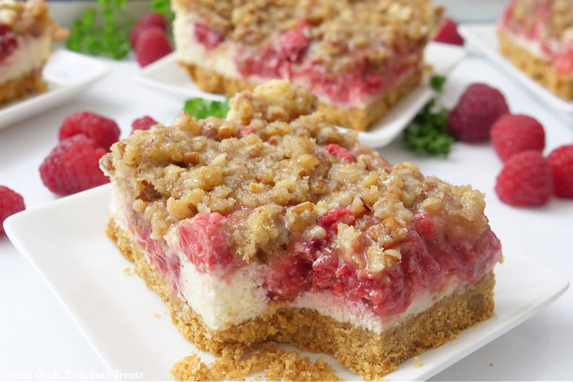 A white plate with a raspberry cheesecake bar on it with a bite taken out with more bars on plates in the background.