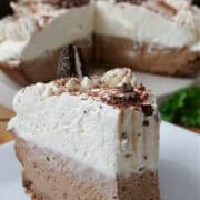 A slice of chocolate cream pie on a white plate with the full pie in the background.