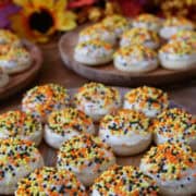 A couple round wood plates with bite-size sugar cookies with frosting and candy sprinkles on them.