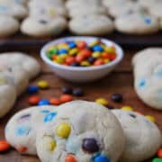 A wood surface with over a dozen bite-sized sugar cookies and mini M&Ms in a small white bowl.