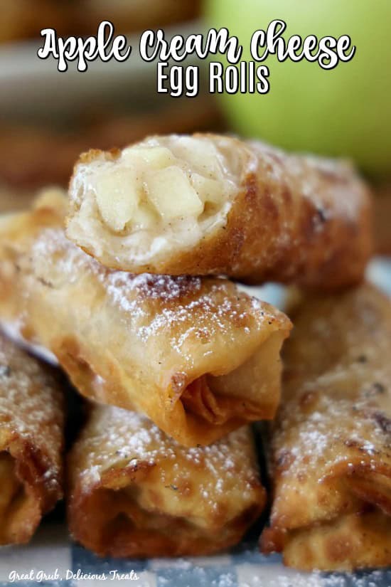 Apple Cream Cheese Egg Rolls are a delicious dessert egg roll recipe filled with a homemade apple filling, a cream cheese mixture, then fried to perfection and the sprinkled with powdered sugar. A stack of five apple egg rolls on a blue and white checkered plate.
