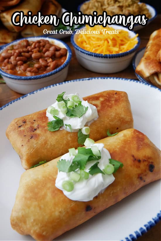 A white plate with blue trim with two fried chicken chimichangas on it topped with sour cream, green onions, and cilantro.