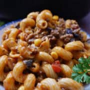 A white bowl with blue trim filled with a serving of beef enchilada pasta with ground beef, corn, black beans, and more.