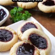 A wood surface with thumbprint cookies on a white square plate and a wire rack in the background filled with cookies.