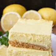 Two lemon cheesecake bars stack on top of each other placed on a white plate.