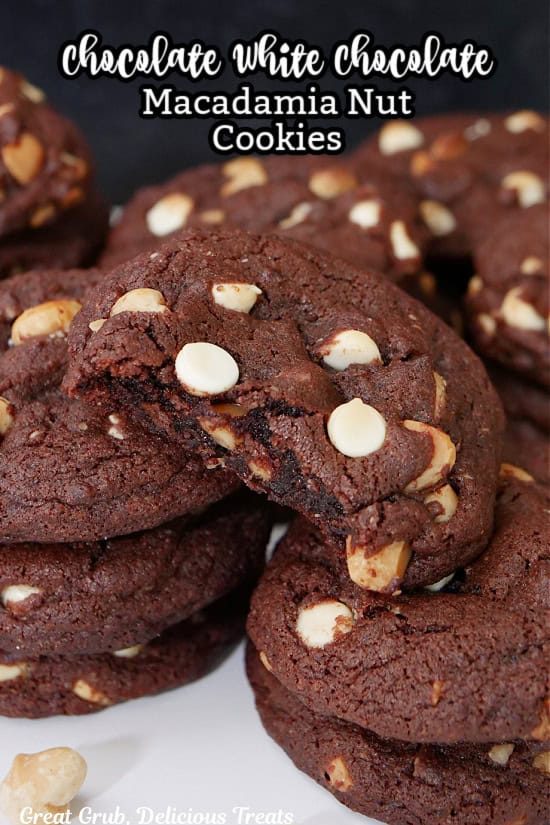 Stacks of chocolate white chocolate macadamia nut cookies on a white surface with a bite taken out of one of them.