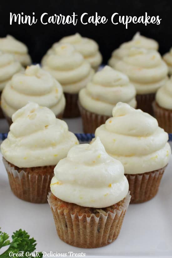 A white surface with mini carrot cake cupcakes on it with orange buttercream frosting on each cupcake.