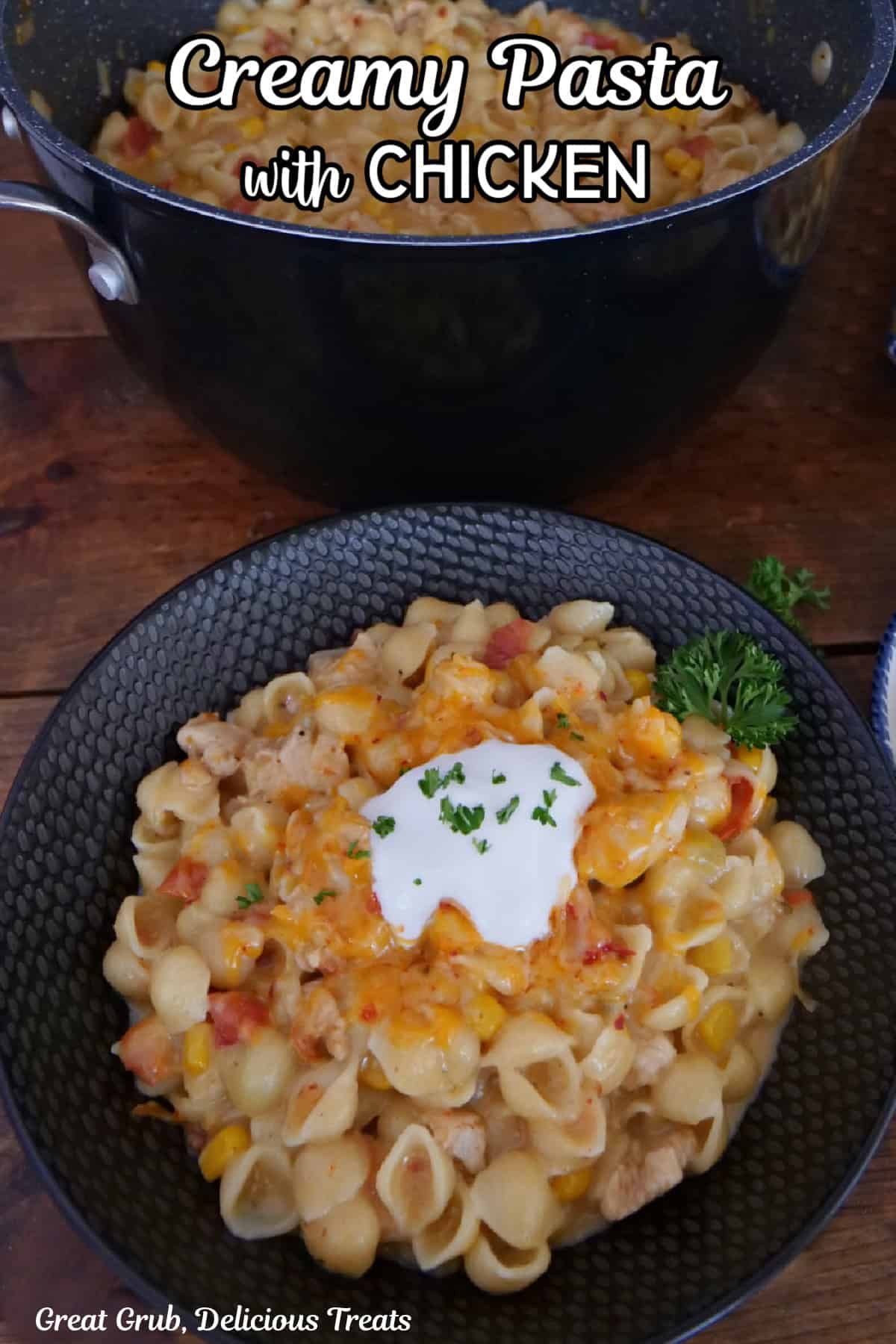 A wood surface with a black bowl filled with a serving of creamy chicken pasta.