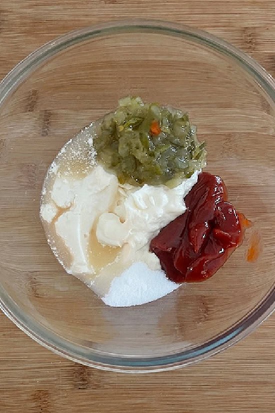 A glass mixing bowl on a wood surface with the ingredients to make the copycat spread in it.