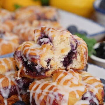A white plate with blue trim with a small stack of blueberry crescent cream cheese muffins with a title overlay at the top.