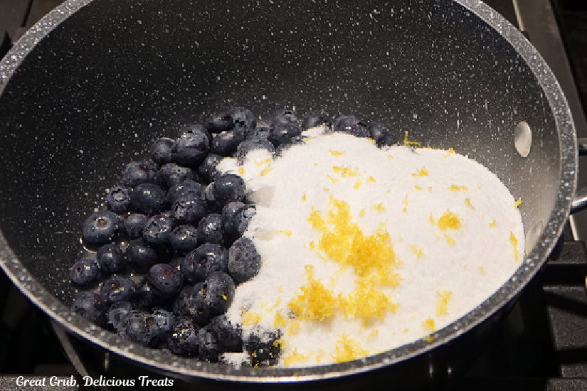 A saucepan with fresh blueberries, sugar, lemon zest, and lemon juice in the pan.