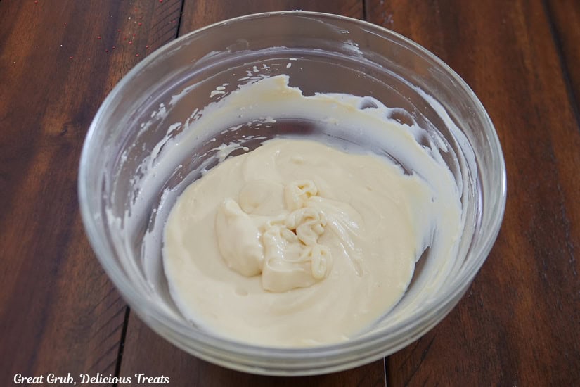 A glass bowl filled with a sweet cream cheese mixture in it on a wood tabletop.