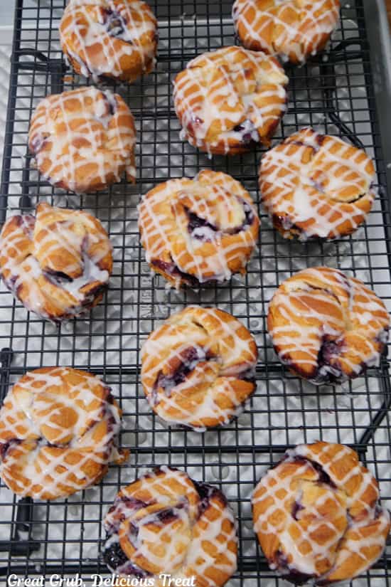 A wire rack with 12 blueberry cream cheese muffins on it with lemon glaze drizzled over them.