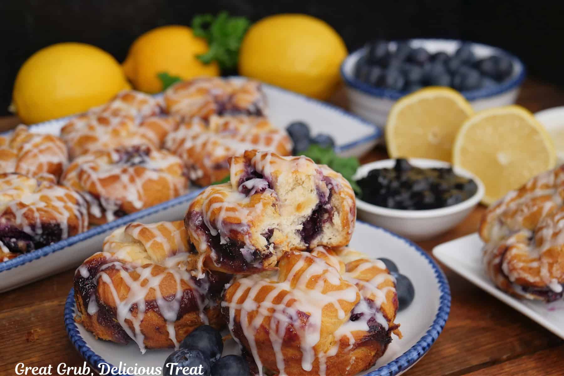 A wood surface with two white plate with blue trim with blueberry crescent cream cheese muffins on them.