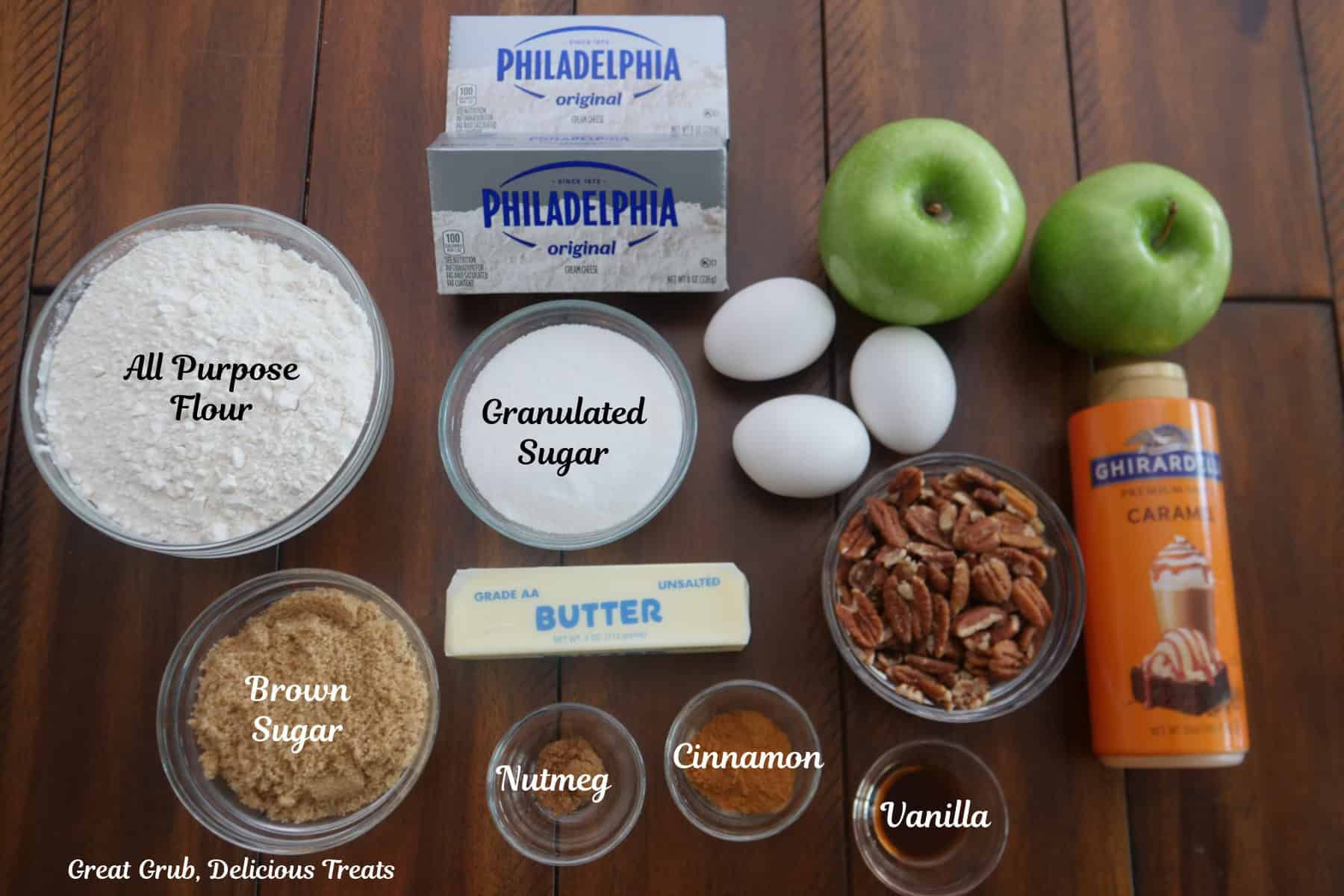 A wood surface with all the ingredients on it to make caramel apple cheesecake bars.