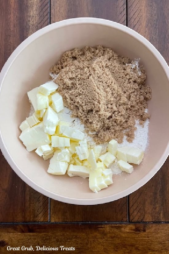 A wood surface with a light pink bowl with flour, sugar,