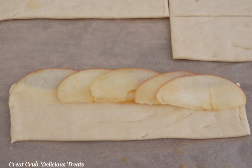 A parchment lined countertop with a crescent dough strip on it with thinly sliced apples placed on it.
