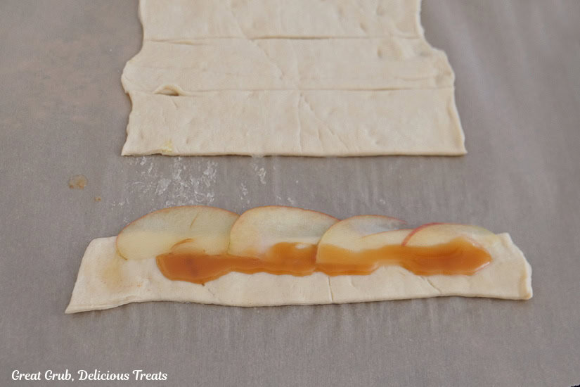 Parchment paper with a strip of crescent dough with apple slices and caramel on the apple slices.