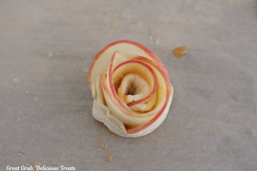 A rolled up crescent dough roses on a piece of parchment paper.
