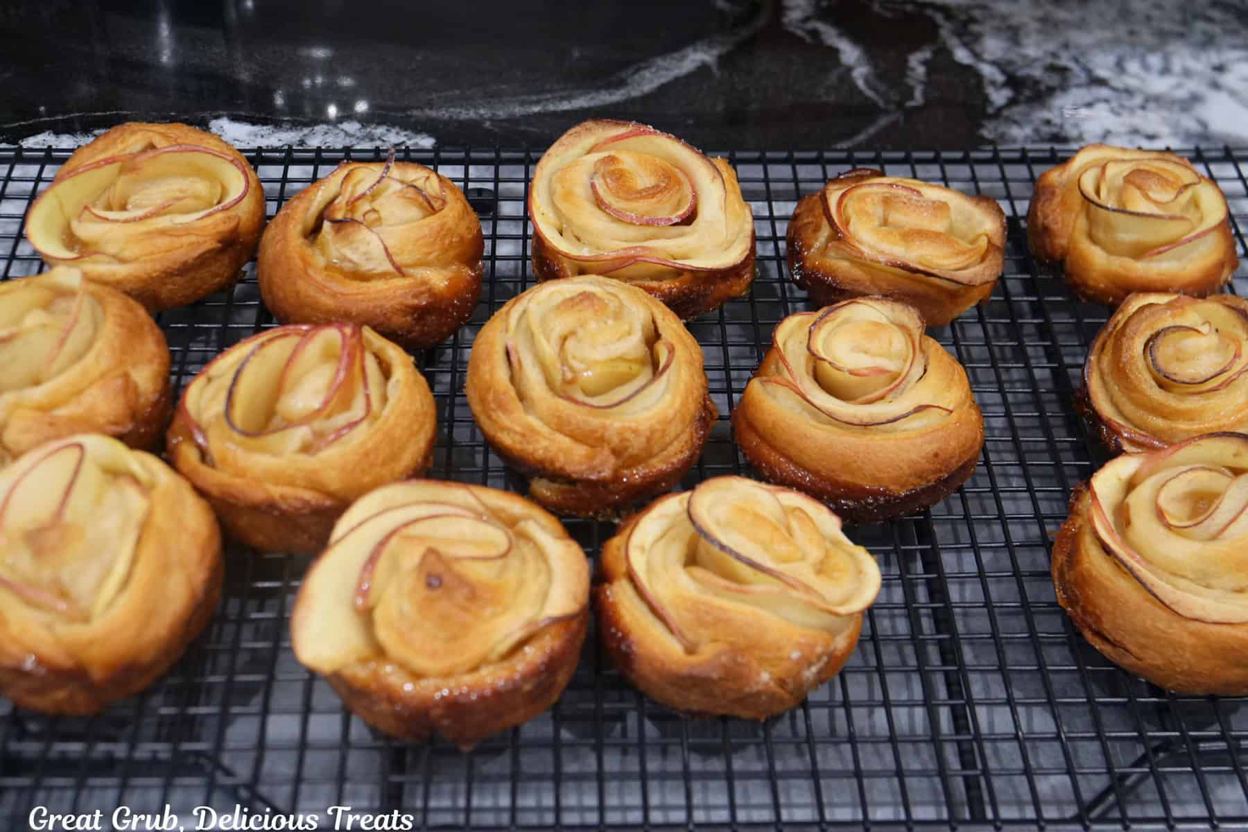 A wire rack with 14 baked caramel apple roses on it right after being removed from the oven.