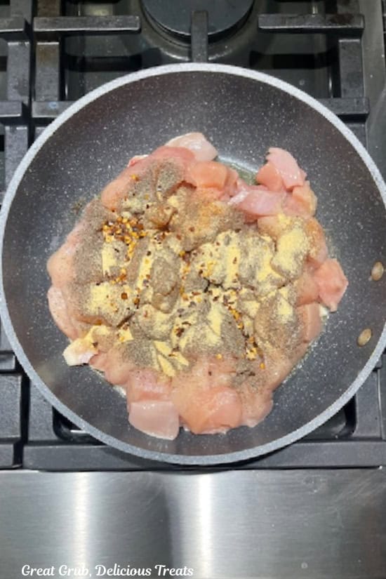 A pan with chicken pieces and seasonings in it as it starts to cook.