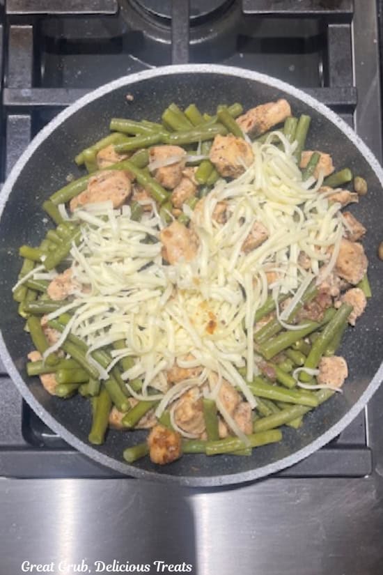 A pan with chicken, green beans, and shredded cheese in it.
