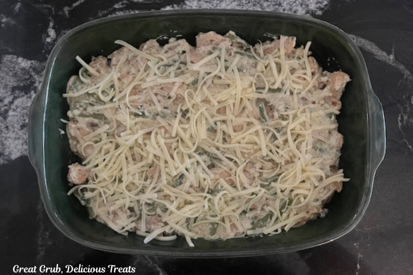 A dark green baking dish filled with cheesy chicken, green beans, cheese, and sauce.