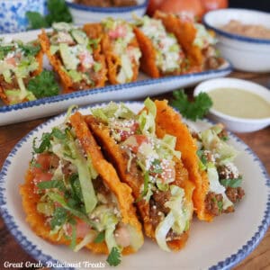 A round white plate with blue trim with three mini cheesy crunch tacos on it.