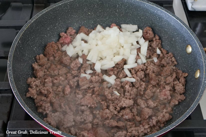 A frying pan with ground beef and diced onions in it.