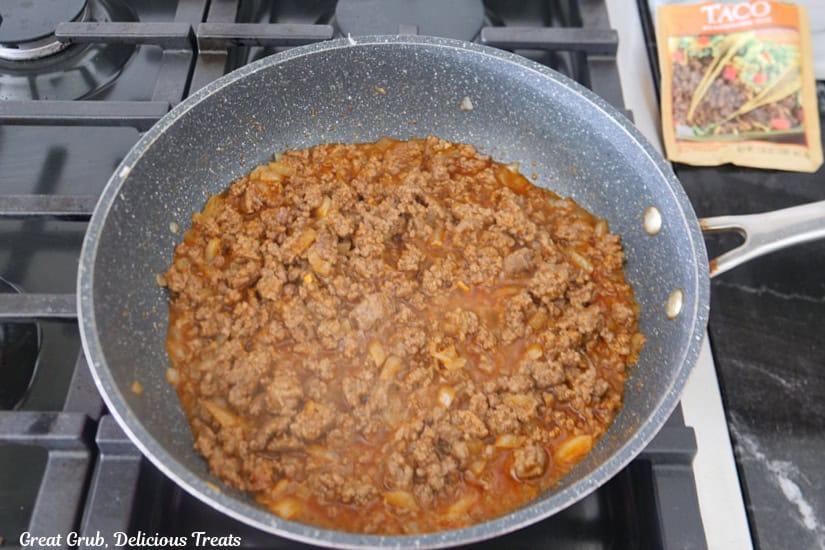 A frying pan with cooked ground beef and taco season packet mixed in.