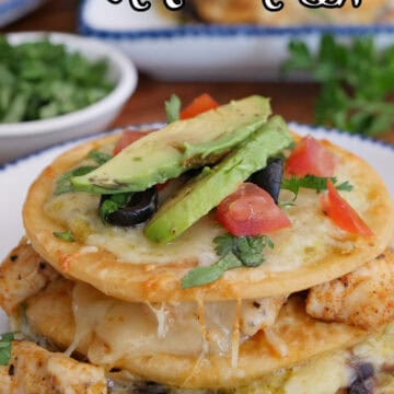 A round white plate with blue trim with a mini three layered Mexican pizza with chicken black beans, cheese, green sauce, and more.